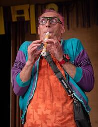 Vergrößerte Ansicht von Nahaufnahme von einem Mann, der Blockflöte spielt. Er schaut etwas verängstigt zur linken Seite.