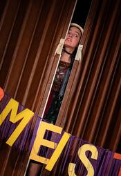 Vergrößerte Ansicht von Eine Frau mit braunen Haaren schaut durch einen Türschlitz hindurch und beobachtet etwas.