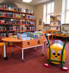 Vergrößerte Ansicht von Niedrige Kisten mit Bilderbüchern, Regale mit Kinderomanen und eine Sitzraupe in der Zweigstelle Seckenheim.