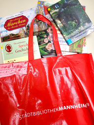 Vergrößerte Ansicht von Verschiedne Bücher ragen aus einer roten Tragetasche mit dem Schriftzug &quot;Stadtbibliothek Mannheim&quot; heraus.