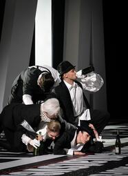 Vergrößerte Ansicht von Vier Personen in historischer Kleidung liegen aufeinander, zwei halten Weinflaschen, eine trägt eine weiße Rüschenkragen und Handschuhe.