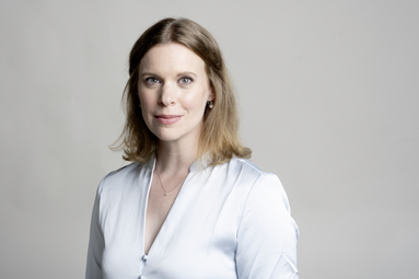 Vergrößerte Ansicht von Jeanette Limbeck steht vor einem einfarbigen Hintergrund und schaut in die Kamera.