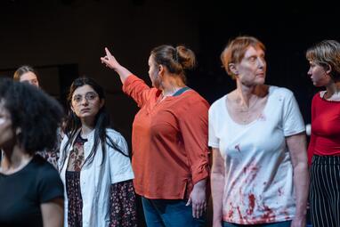 Vergrößerte Ansicht von Einige Frauen stehen eng beieinander und schauen in verschiedene Richtungen. Eine von ihnen streckt hren Arm in die linke Blickrichtung und zeigt auf ein uns unbekanntes Ziel.