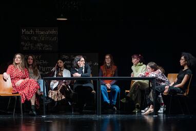 Vergrößerte Ansicht von Die Frauen sitzen um einen Tisch. Einige stützen gelangweilt ihre Arme und Köpfe auf den Tisch.