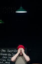 Vergrößerte Ansicht von Eine Person steht alleine unter einer Lampe. Sie hält die Hände vor den Augen