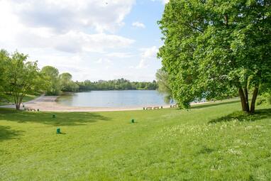 Vergrößerte Ansicht von Eine Liegewiese mit Bäumen, im Hintergrund der Vogelstang-See.