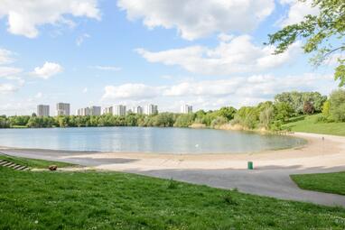 Vergrößerte Ansicht von Die Badestelle am Unteren Vogelstang-See mit Sandstrand. Im Hintergrund Hochhäuser.