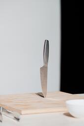 Vergrößerte Ansicht von Ein silbernes Messer steht auf seiner Spitze auf einem Holzbrett.