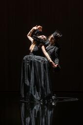 Vergrößerte Ansicht von Zwei Personen in schwarzer Bühnenkleidung mit Kronen tanzen eng umschlungen vor dunklem Hintergrund