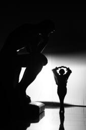 Vergrößerte Ansicht von Silhouette einer Statue in Denkpose neben einer tanzenden Person mit erhobenen Armen vor hellem Hintergrund