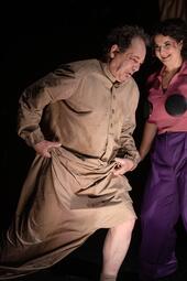 Vergrößerte Ansicht von Person in langem, beigem Kleid mit Knöpfen und gerafftem Saum, die sich nach vorne beugt, daneben eine Person in lila Hose und rosa Oberteil mit schwarzen runden Applikationen