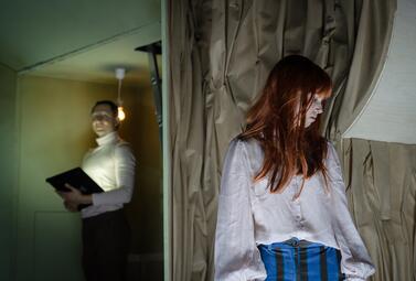 Vergrößerte Ansicht von Zwei Frauen in einem Raum, eine im Vordergrund mit langem roten Haar und weißer Bluse, die andere im Hintergrund mit Tablet in der Hand