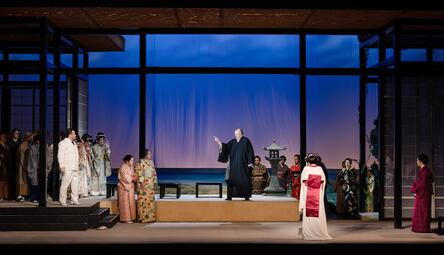 Vergrößerte Ansicht von Bühnenbild mit mehreren Personen in traditioneller asiatischer Kleidung vor blauem Hintergrund und Meeresszenerie