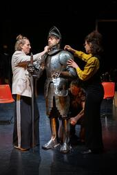 Vergrößerte Ansicht von Vier Personen. Der Mann in der Mitte trägt eine Ritterrüstung. Drei weitere Personen helfen ihm, diese Rüstung anzuziehen.