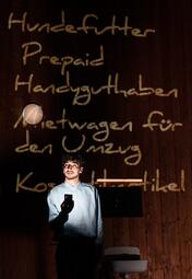 Vergrößerte Ansicht von Person in weißem Hemd steht vor einer dunklen Wand mit handgeschriebener Liste aus hellen Buchstaben