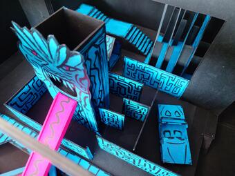 Vergrößerte Ansicht von Modell eines Labyrinths mit blauen Wänden und einem Drachenkopf mit rotem Auge, aus dessen Maul eine pinke Zunge herausragt