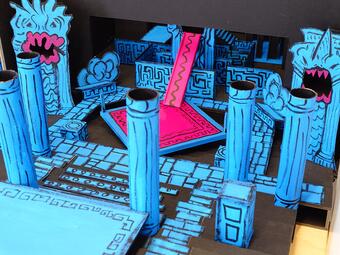 Vergrößerte Ansicht von Modell einer antiken Tempelanlage mit blauen Säulen, roten Treppen und stilisierten Flammenmotiven