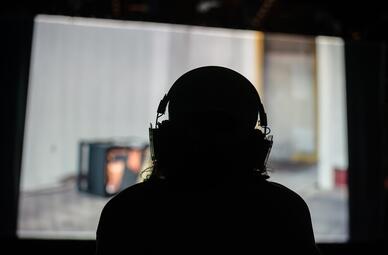 Vergrößerte Ansicht von Silhouette einer Person mit Kopfhörern vor einem unscharfen Bildschirm in einem dunklen Raum