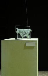 Vergrößerte Ansicht von Altes tragbares Radio mit gehäkelter Spitze auf einem weißen Podest vor schwarzem Hintergrund