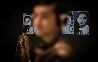 Vergrößerte Ansicht von Person steht vor einer Wand mit mehreren schwarz-weißen Porträtfotografien