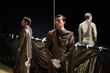 Vergrößerte Ansicht von Person in glänzendem, langem Gewand mit weißen Handschuhen steht vor einem Spiegel, der eine Rückansicht zeigt