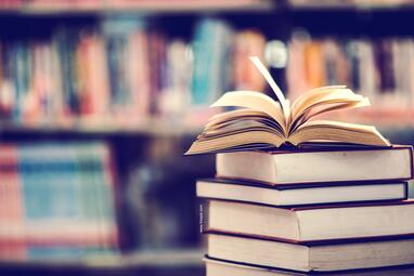 Vergrößerte Ansicht von Ein aufgeschlagenes Buch liegt auf einem Stapel Bücher.