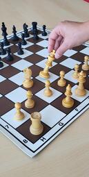 Vergrößerte Ansicht von Ein Schachbrett und eine Hand, die eine Spielfigur bewegt