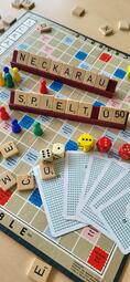 Vergrößerte Ansicht von Auf einem Tisch liegen, Spielkarten, Würfel und ein Scrabble-Spiel. Mit den Buchstaben des Spiels wurde der Text "Neckarau spielt Ü50" gebildet.