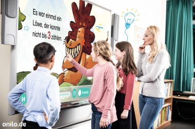 Vergrößerte Ansicht von mehrere Kinder und eine Frau stehen vor einem Bildschirm und schauen sich die Boardstory "Vom Löwen, der nicht zählen konnte" an.