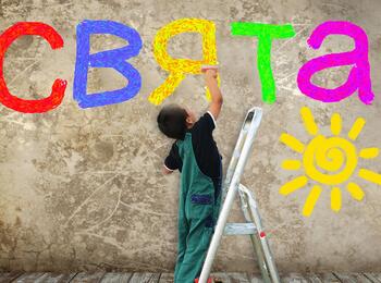 Ein Kind schreibt mit einem Malerpinsel Buchstaben an eine Hauswand