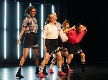 Während des Schwindelfrei Festival 2024 wird das Stück "Radical Cheerleading“ von Zufit Simon im EinTanzHaus präsentiert. Zu sehen sind fünf Personen, die in sportlicher Kleidung mit entschlossenem Blick auf der Bühne stehen.