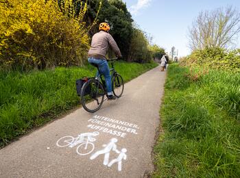 Fahrrad fährt auf Radweg. Kreidespray auf Fahrbahn weist auf ein rücksichtsvolles Miteinander hin