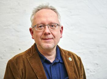 Henner Kallmeyer, kurze graue Haare, brille, braune Jacke, von der Brust aufwärts fotographiert, lächelt in die Kamera.