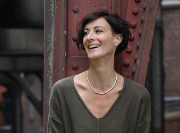 Tania Witte lehnt an einer Säule, lacht und schaut dabei zur Seite.