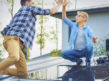 Mann und Kind installieren Solaranlage auf Dach und klatschen sich ab