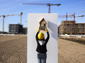 Frau mit Bauhelm hängt in einer Baustelle ein Vogelnistkasten auf