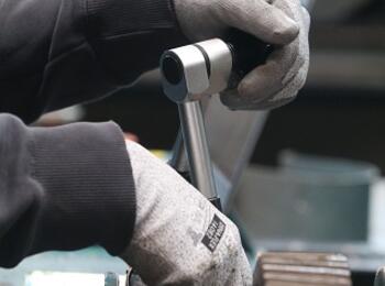 Nahaufnahme eines Mechanikers, der einen Schraubenschlüssel verwendet, um Maschinen einzustellen, und damit die industrielle Arbeit hervorhebt.