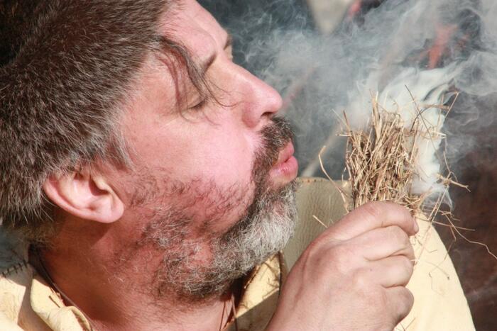 Mann bläst auf ein brennendes Strohbüschel