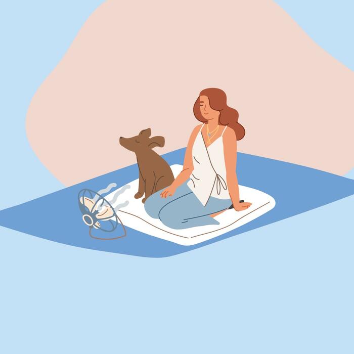 Eine Frau sitzt gemeinsam mit einem Hund auf einer Picknickdecke.