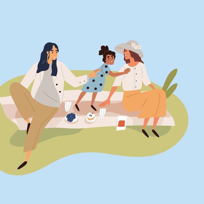Eine Mann und eine Frau sitzen gemeinsam mit einem kleinen Mädchen auf einer Decke im Freien und picknicken. 