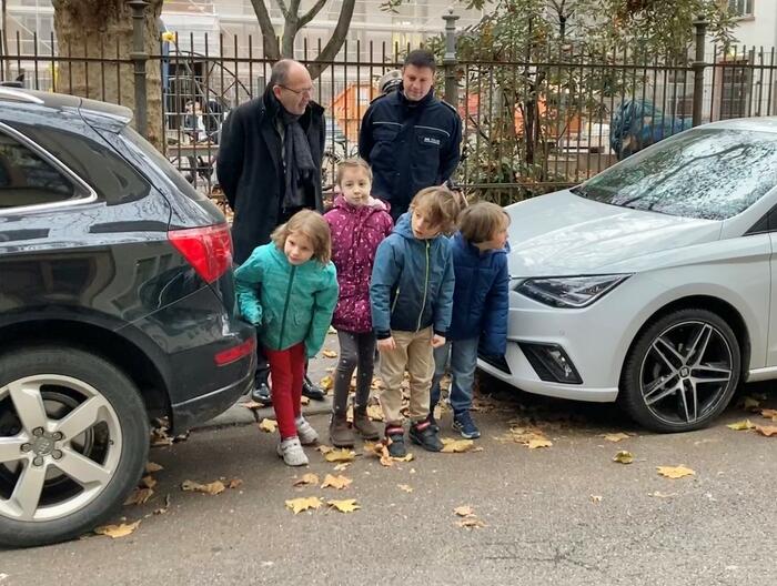 Erstklässler üben mit Polizei und Erstem Bürgermeister Specht das Überqueren der Straße zwischen geparkten Autos.