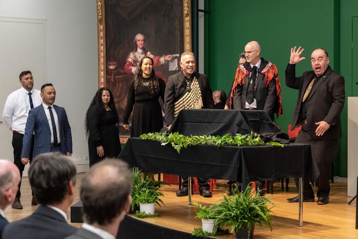 Tisch auf einer Bühne mit schwarzer Abdeckung, dahinter mehrere Mitglieder einer Maori-Delegation