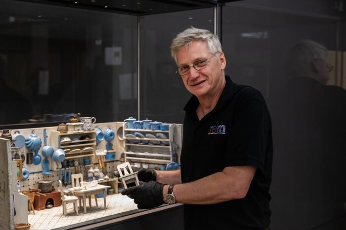 Mann stellt einen Stuhl in eine große Puppenküche