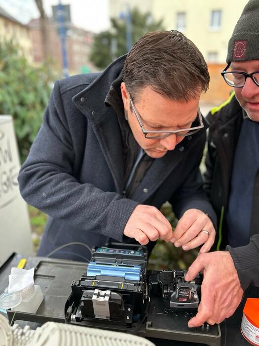 Arbeiten am Glasfaser-Kabel: Bürgermeister Dr. Volker Proffen darf sich unter fachkundiger Anleitung selbst im Spleißen versuchen.