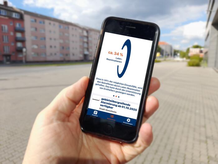Eine Hand hält ein Handy. Der Bildschirm zeigt die App Katretter mit einem Hinweis zur Laien-Reanimation