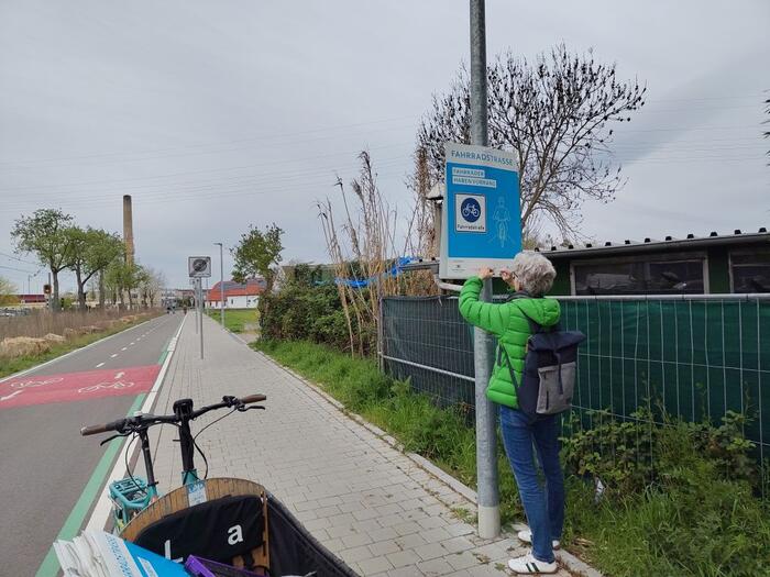 Person hängt Plakat der Aktion Rücksichtnahme auf Mannheims Fahrradstraßen am Rand einer Fahrradstraße auf